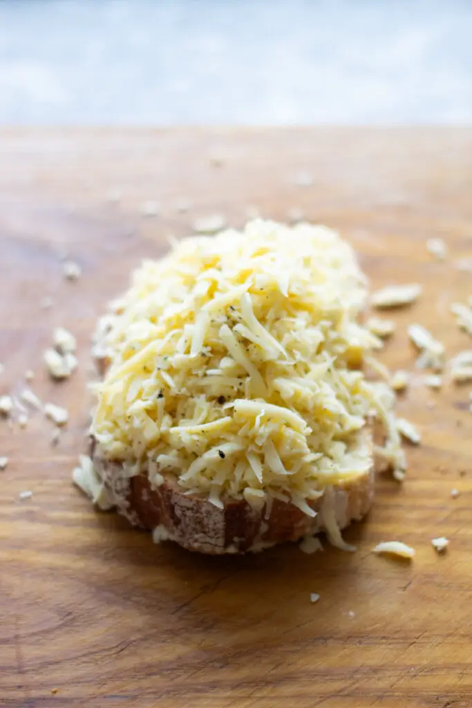A generous mound of grated cheese piled on a slice of sourdough bread before making a grilled cheese.