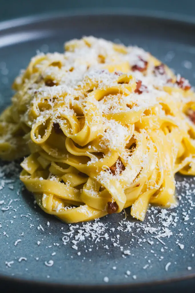 Tagliatelle carbonara served on a dark plate with grated cheese