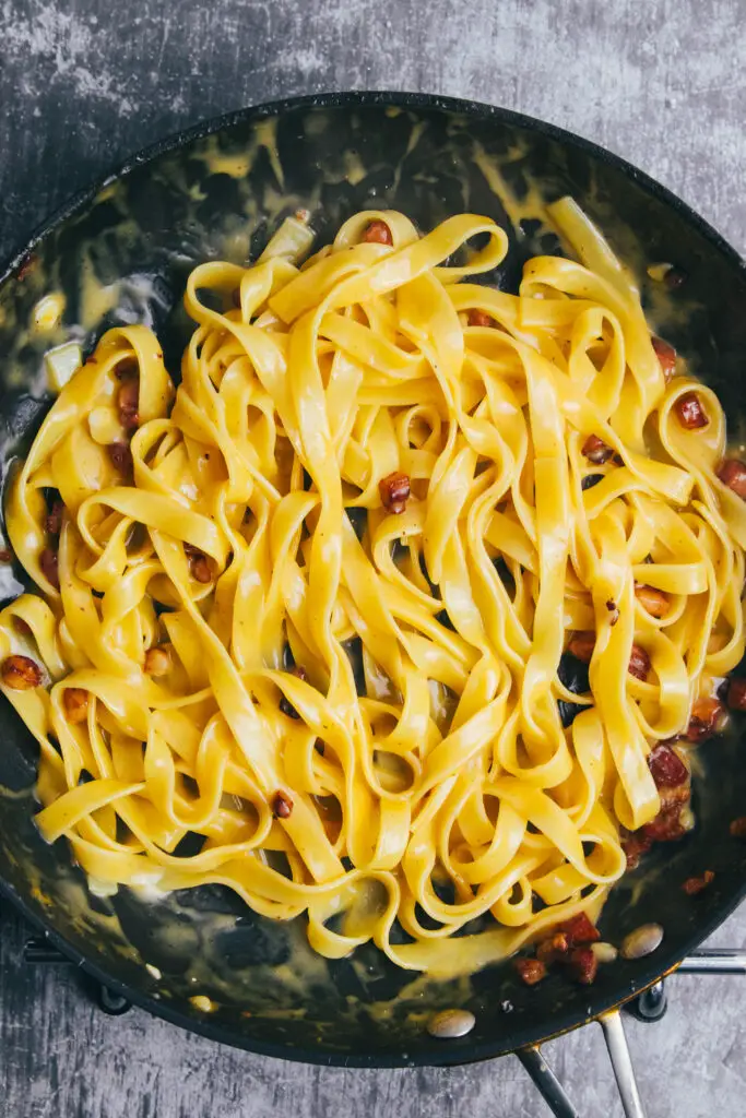 Tagliatelle being tossed in a creamy carbonara sauce with pancetta