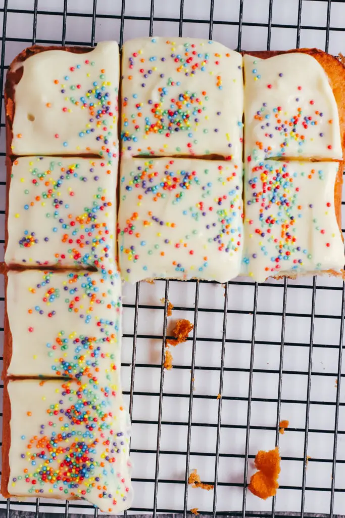 Iced vanilla traybake cut into squares and arranged on a cooling rack.